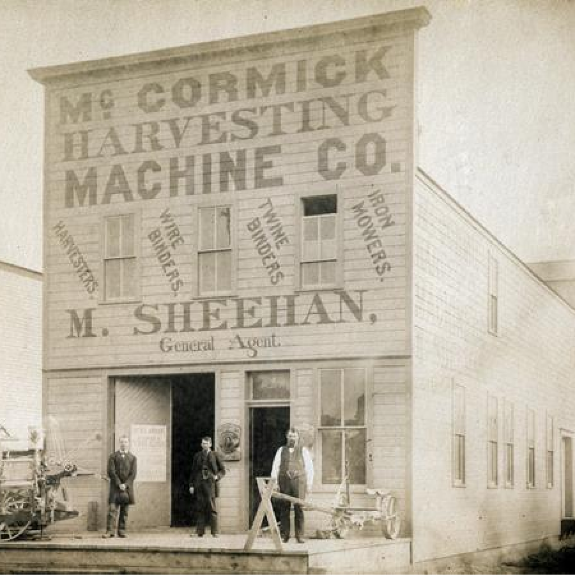 Image: Three men posing with a McCormick mower and binder in front of M. Sheehan's McCormick Harvesting Machine Company dealership.