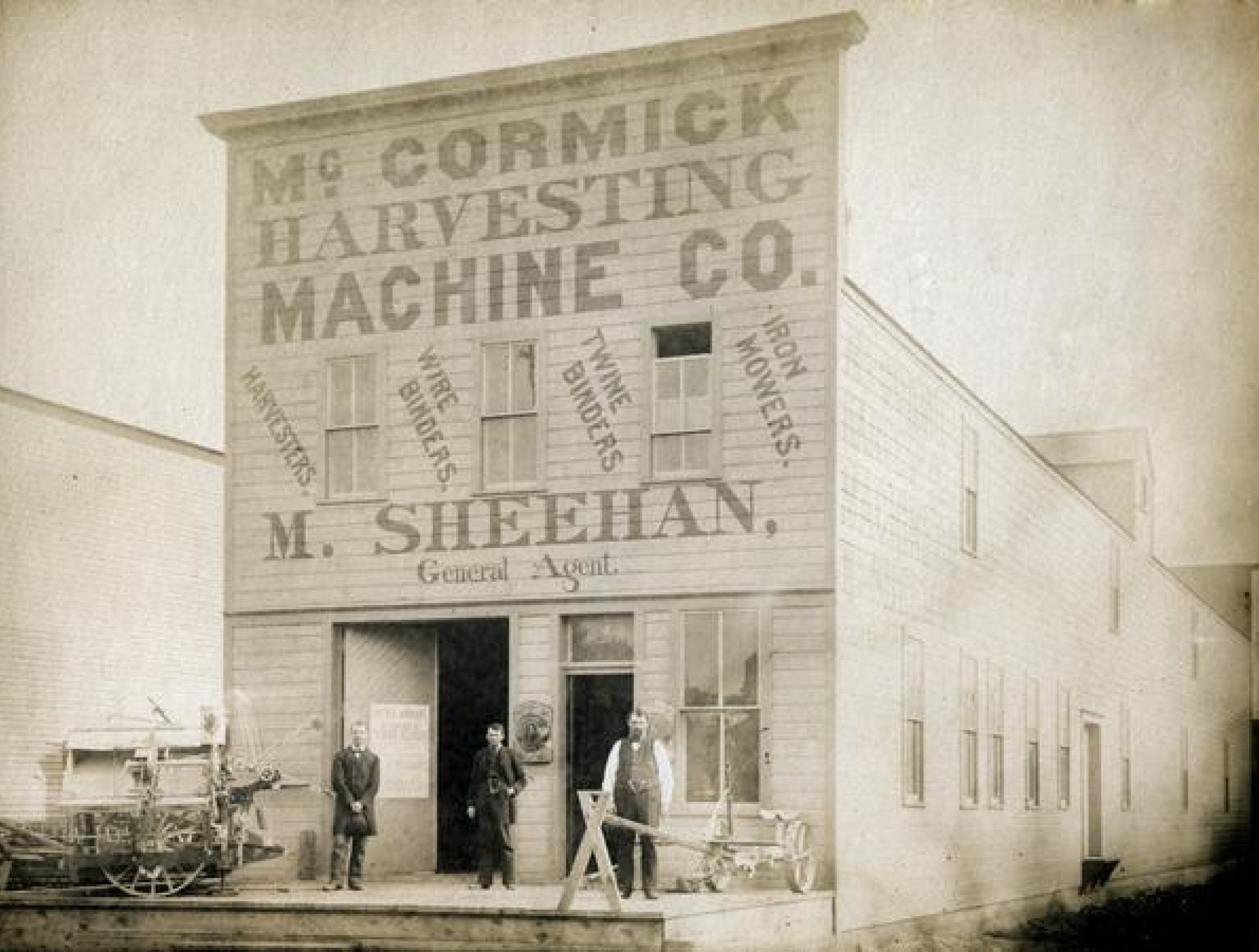 Image: Three men posing with a McCormick mower and binder in front of M. Sheehan's McCormick Harvesting Machine Company dealership.