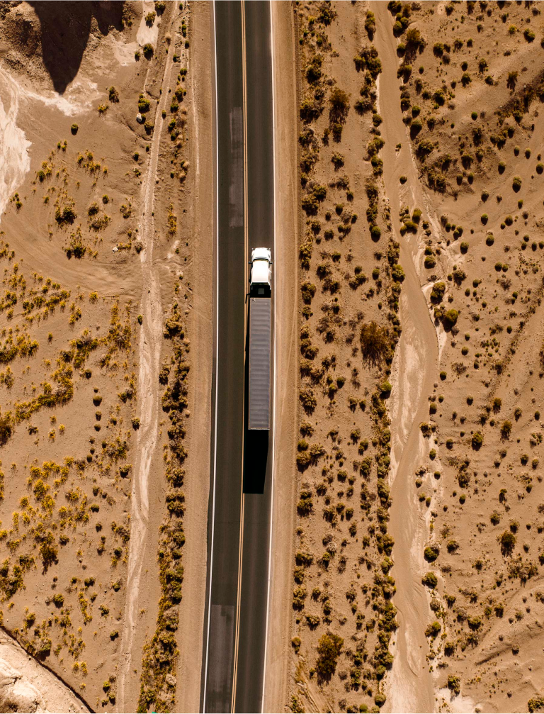 A birds eye view of a truck on the motorway moving through a desert canyon