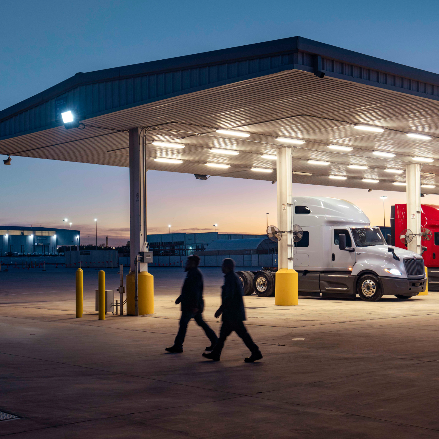 Two men walking in front of gas station at night